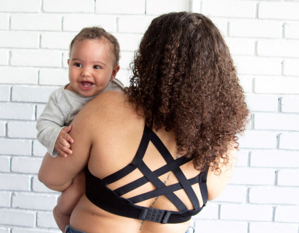 Back of woman wearing black strappy nursing bra holding a baby